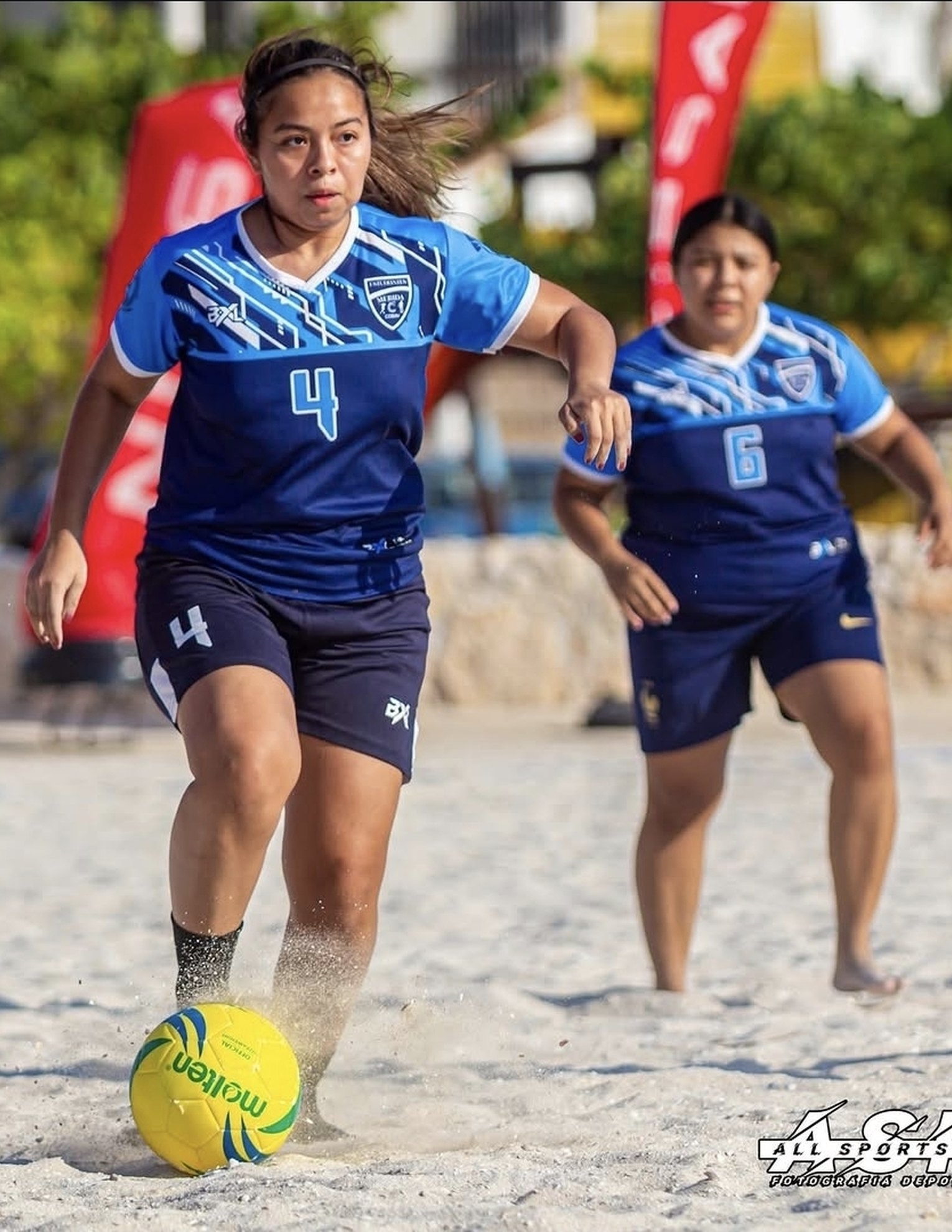 Jugadoras de fútbol playa con uniformes BXL en rojo y negro, listas para el partido